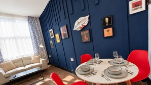 Un coin repas avec une table ronde pour quatre personnes, des chaises rouges et un mur d’accent bleu orné d’œuvres d’art encadrées.