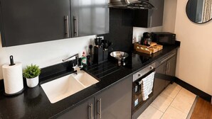 Une cuisine moderne avec des meubles de rangement noirs, des appareils en acier inoxydable, un plan de travail noir et une petite plante en pot.