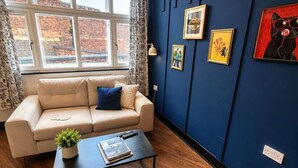 Un salon moderne avec un canapé beige, une table basse et un mur d’accent bleu orné de tableaux encadrés.