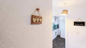 A hallway with a textured wall, a hanging heart-shaped decoration, a kitchen area with a washing machine, and a sign that reads "THIS IS OUR Happy peace". - Wycombe Oasis - Cozy 3-bed House Retreat (High Wycombe)