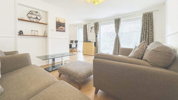A modern living room with a sofa set, a glass coffee table, and a dining area with a table and chairs. - Wycombe Oasis - Cozy 3-bed House Retreat (High Wycombe)
