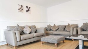 A modern living room with a grey sofa set, patterned cushions, and a glass coffee table. - Wycombe Oasis - Cozy 3-bed House Retreat (High Wycombe)