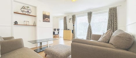 Una sala moderna con un sofá, un reposapiés y una mesa de centro de vidrio.