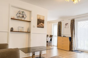 A modern living room with a glass-top table, a sofa, a wooden dresser, and a dining area in the background. - Wycombe Oasis - Cozy 3-bed House Retreat (High Wycombe)