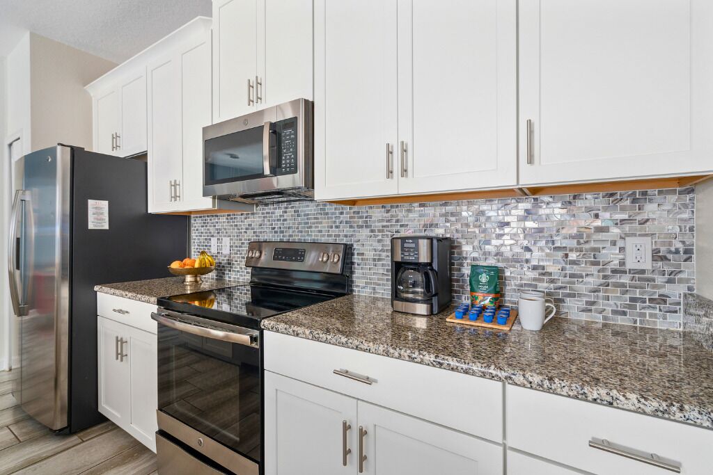 A modern kitchen with white cabinets, stainless steel appliances, a tiled backsplash, and a granite countertop.