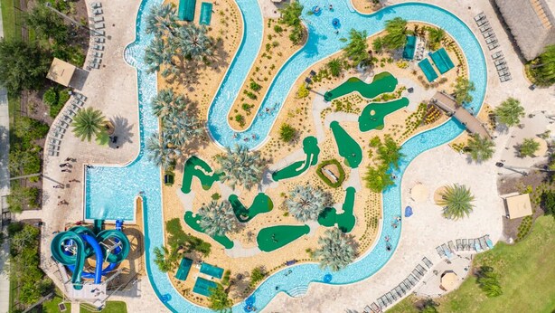 An aerial view of a resort with multiple swimming pools, a water slide, and sun loungers. - Gatsby Gamehouse (Kissimmee)