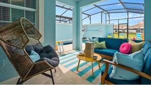 A sunlit indoor space with a blue and white color scheme, featuring a wicker chair, a blue sofa, and a small table with a box and a bowl. - Gatsby Gamehouse (Kissimmee)