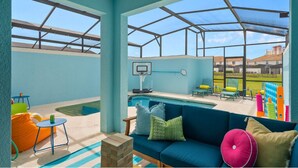 An indoor pool area with a blue couch, colorful chairs, and a basketball hoop. - Gatsby Gamehouse (Kissimmee)