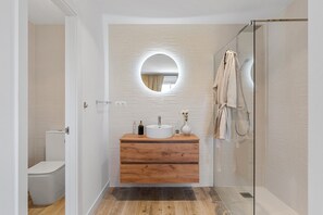 Ein modernes Badezimmer mit einem Holzwaschtisch, einem runden Spiegel und einer Duschkabine aus Glas.