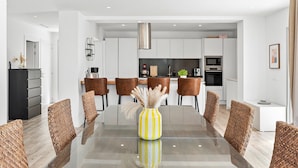 Un comedor moderno con una mesa de vidrio, sillas tejidas color marrón y un jarrón amarillo con plumas de pámpano.