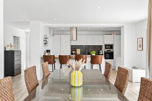 A modern dining area with a glass table, brown woven chairs, and a yellow vase with pampas grass.