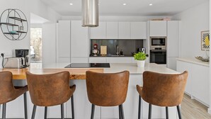 Una cocina moderna con armarios blancos, una isla central y taburetes de bar.
