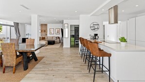Una cocina moderna con barra, una mesa de comedor con sillas y una sala de estar con sofá y televisor.