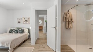 Un dormitorio con cama, mesita de noche, espejo y baño con ducha y toallero.