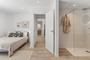 Une chambre à coucher comprenant un lit, une table de chevet, un miroir et une salle de bain avec une douche et un porte-serviettes.