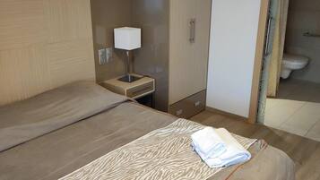 A hotel room with a bed, a nightstand, a lamp, a wardrobe, and a bathroom visible through an open door.