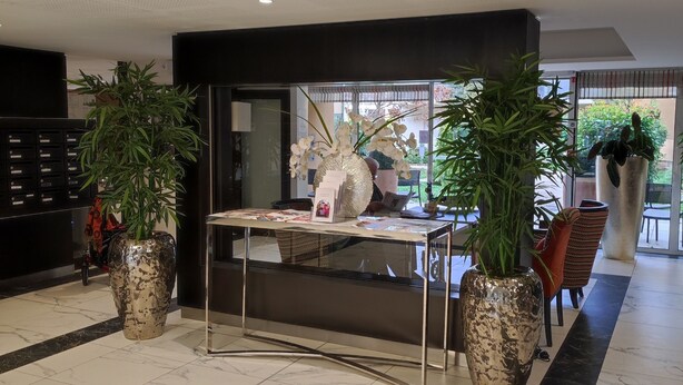 A reception area with a marble-tiled floor, a reception desk, and large potted plants. - Appart One Uzès (Uzès)