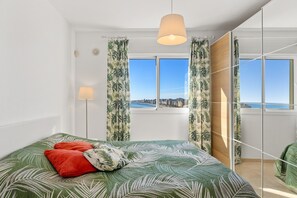 Een slaapkamer met een bed, een vloerlamp, een raam met gordijnen en uitzicht op de stad.