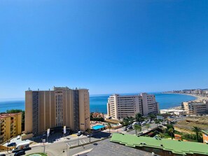 Un paysage urbain côtier avec de hauts immeubles, un ciel bleu dégagé et une plage au loin.