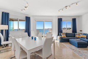 Een moderne woonkamer met een eetgedeelte, grote ramen met uitzicht op zee en een balkon.