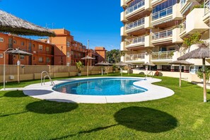Une piscine entourée de pelouse, avec un bâtiment en arrière-plan.
