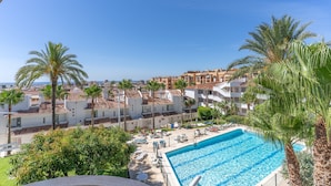 A swimming pool with lounge chairs, palm trees, and a view of a coastal town with buildings. - Apartment in Los Pacos, Fuengirola (Fuengirola)