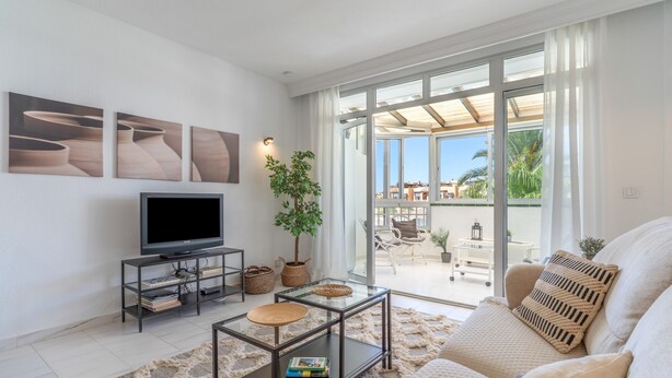 A modern living room with a flat-screen TV, a glass coffee table, a sofa, and a large sliding glass door leading to an outdoor area. - Apartment in Los Pacos, Fuengirola (Fuengirola)