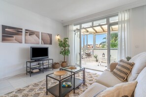 A modern living room with a flat-screen TV, a glass coffee table, a sofa, and a large sliding glass door leading to an outdoor area. - Apartment in Los Pacos, Fuengirola (Fuengirola)