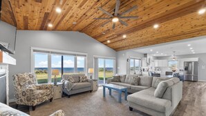 A spacious living room with a large window, a ceiling fan, and a view of the ocean.