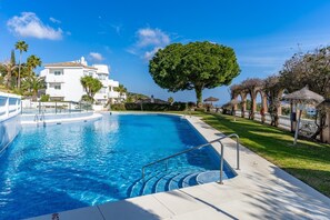 A swimming pool with clear blue water, a white building with balconies, and a large tree in the background. - Apartment in Calahonda, Mijas (Mijas)