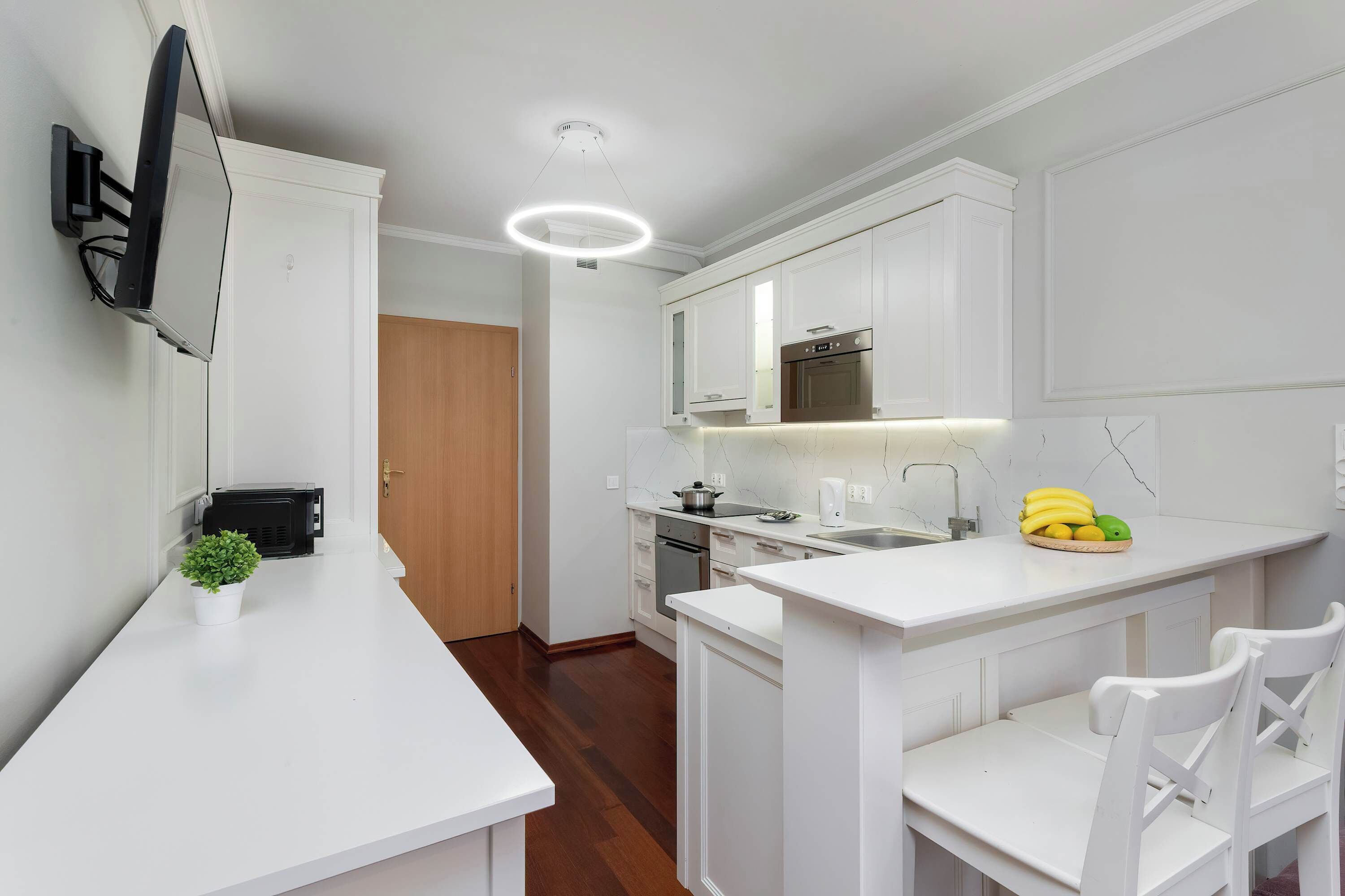 Une cuisine moderne avec des meubles blancs, un four à micro-ondes encastré, une cuisinière et un petit îlot central avec des chaises.