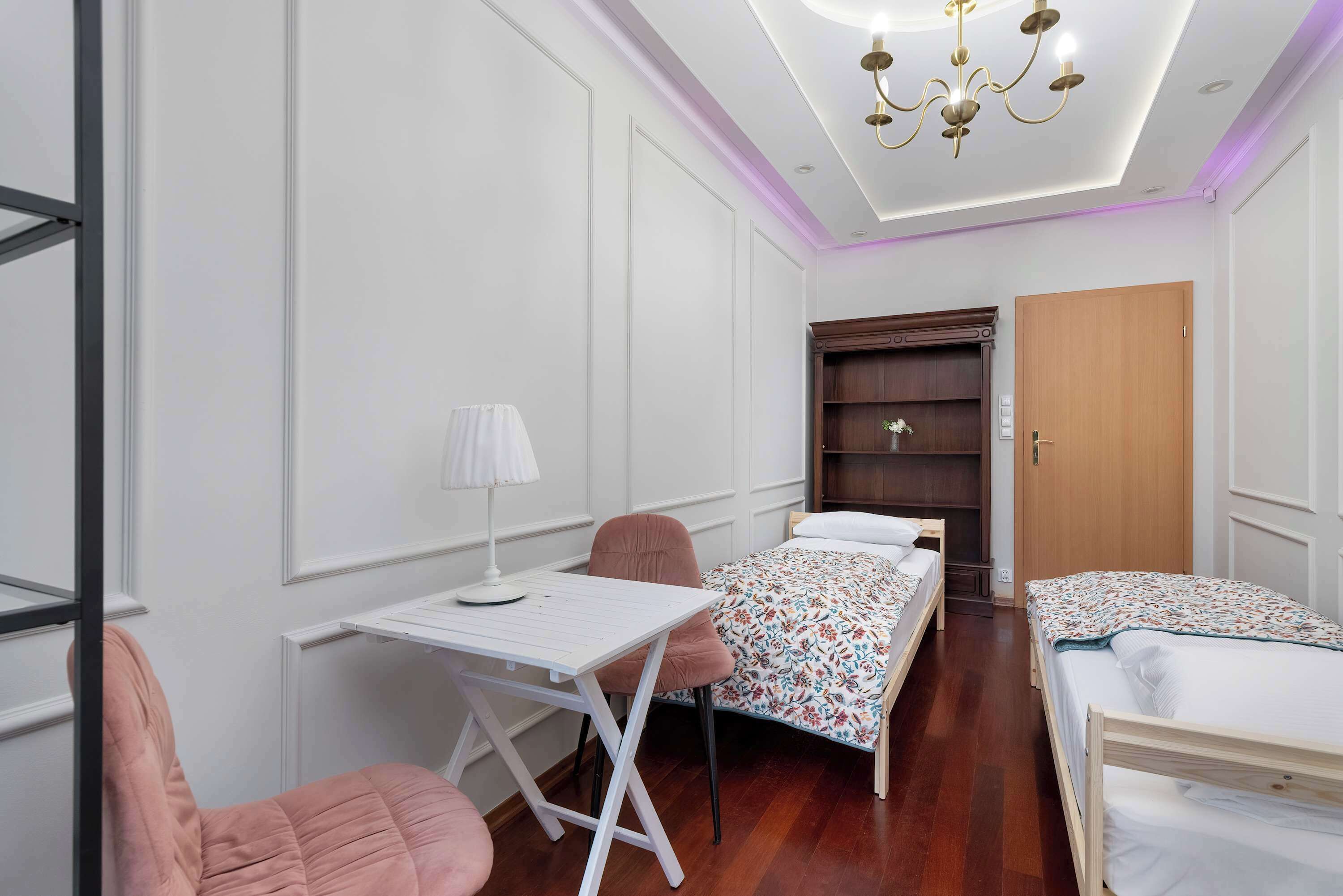 A bedroom with two beds, a desk, a chair, a wardrobe, and a ceiling light.