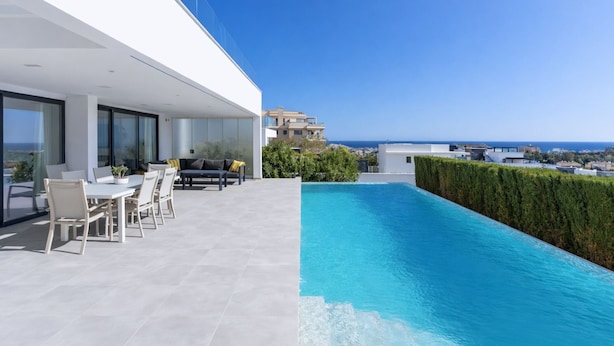 A modern outdoor pool area with a dining set and a view of the sea. - Modern Villa Lynx with Sauna, Heated Infinity Pool, and Garden (Las Lagunas de Mijas)