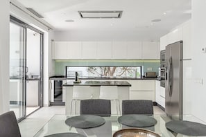 Een moderne keuken met een glazen eethoek, witte kastjes en een roestvrijstalen koelkast.