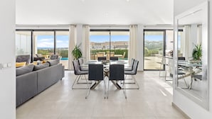 A modern interior with a dining area, sofa, and large windows offering a view. - Modern Villa Lynx with Sauna, Heated Infinity Pool, and Garden (Las Lagunas de Mijas)