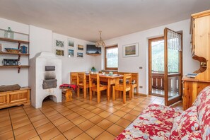 A cozy living room with a fireplace, wooden furniture, and a large window offering a view of the outdoors. - Sports and nature in Trentino! (Vigo di Fassa)