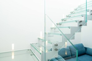 Eine moderne Treppe mit Glasgeländern und einem blauen Sofa im Vordergrund.