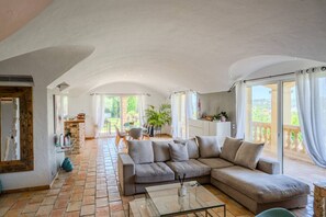 Ein großzügiger Wohnbereich mit einer großen Couch, einem Couchtisch und Blick auf einen Garten durch eine Glastür.