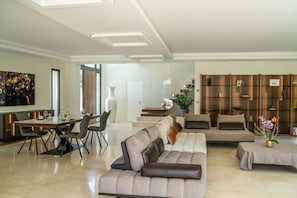Ein modernes Wohnzimmer mit einer Couch, einem Esstisch und Stühlen. Es gibt ein großes Fenster, ein Gemälde und eine Pflanze.