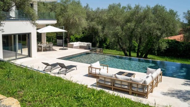 A modern outdoor pool area with a glass-enclosed patio, lounge chairs, and a dining set. - Villa spacieuse avec piscine (Opio)