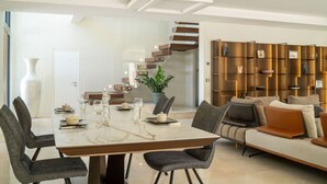 A modern living room with a marble dining table, grey upholstered chairs, a beige sofa, and a wooden bookshelf. - Villa spacieuse avec piscine (Opio)