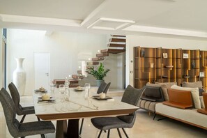 Ein modernes Wohnzimmer mit einem Marmorestisch, grau gepolsterten Stühlen, einem beigen Sofa und einem Holzregal.