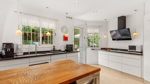 A modern kitchen with a wooden dining table, built-in appliances, and pendant lighting. - Villa with Private Pool, Garden, and Privacy in Cerros del Águila, Mijas (Mijas Costa)