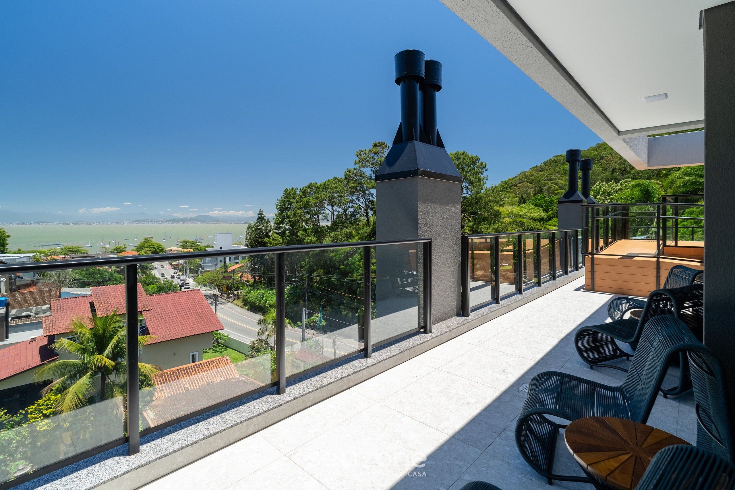 Ein Balkon mit Blick auf eine Küstenlandschaft, Sitzgelegenheiten im Freien und einem Schornstein.