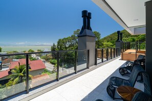 A balcony with a view of a coastal area, outdoor seating, and a chimney. - Estúdio premium com varanda e sol da manhã SGR0217 (Florianópolis)
