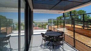 A modern outdoor balcony with a glass railing, a wooden deck, and a table with chairs. - Estúdio premium com varanda e sol da manhã SGR0217 (Florianópolis)