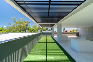 Un espacio al aire libre cubierto con un camino de césped artificial verde, pilares blancos y una vista despejada del paisaje circundante.