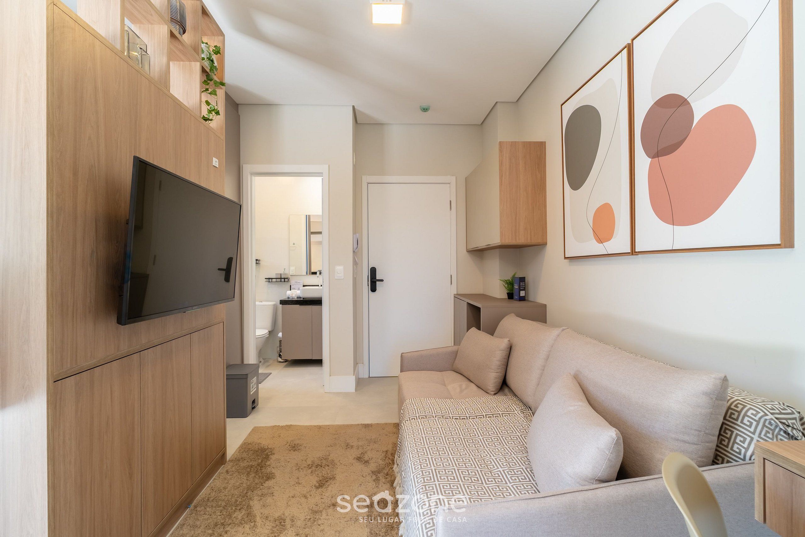 A modern living room with a flat-screen TV, a sofa, and abstract wall art.