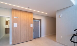 A hallway with a wooden door labeled "HIDROMETROS" and a grey elevator with a patterned door. - Estúdio premium com varanda e sol da manhã SGR0217 (Florianópolis)