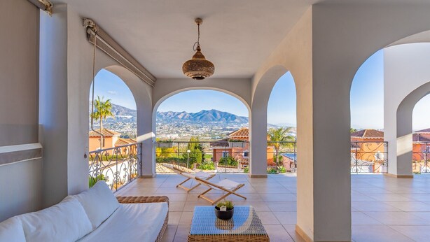 Un balcon avec un canapé blanc, une table basse en osier et un luminaire suspendu.